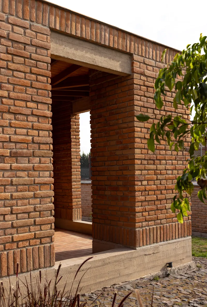 Brick passageway with concrete lintel framing a view through to a distant courtyard at dusk