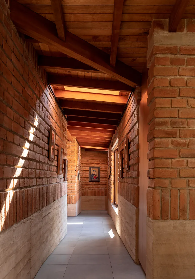 Narrow corridor with exposed brick walls, timber ceiling beams and skylights casting diagonal shadows on the floor