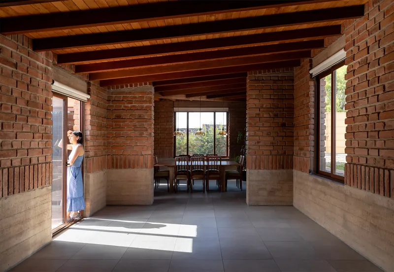 Open living space with brick walls, exposed timber beams and a figure standing in doorway light