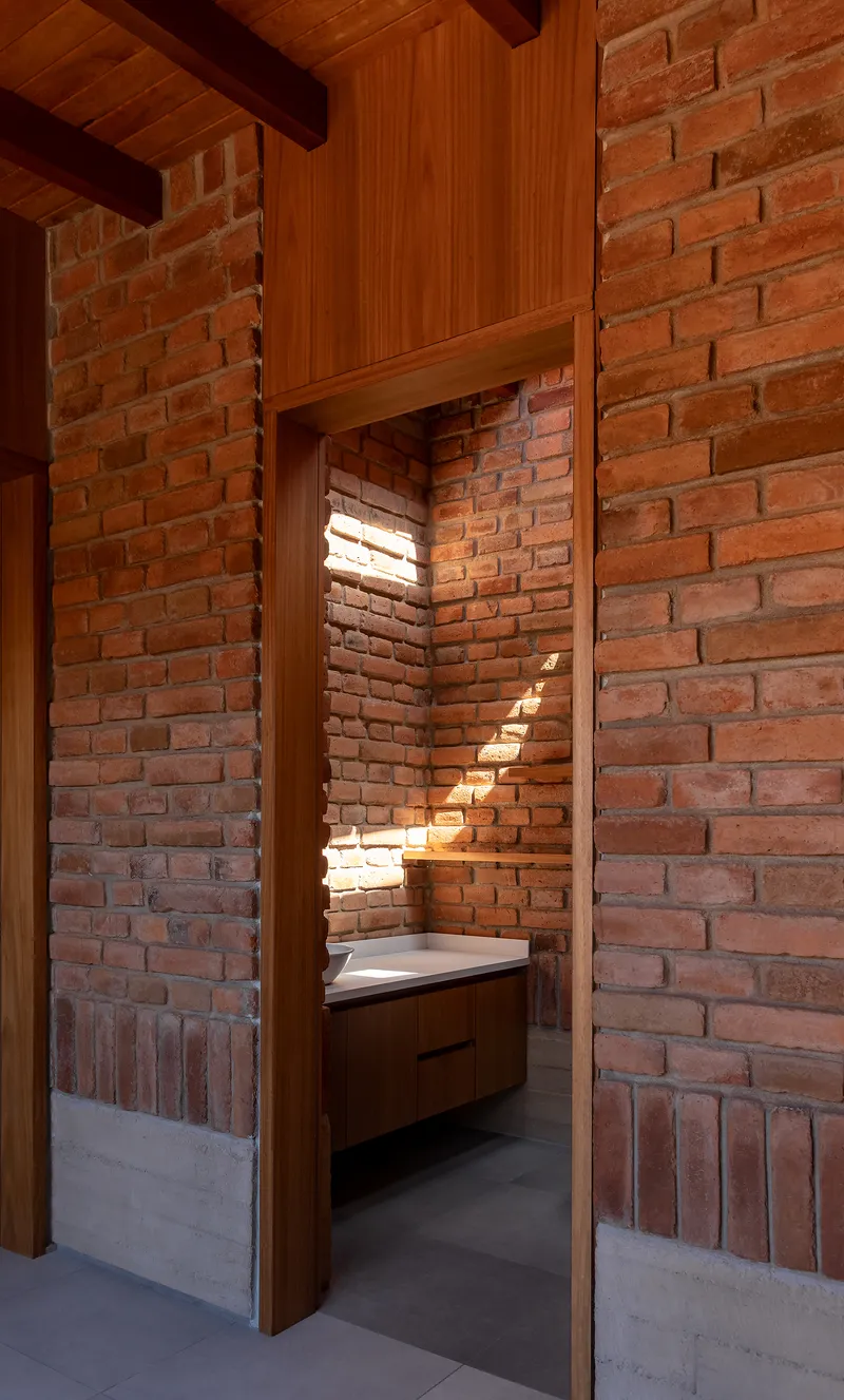 View through timber doorframe into bathroom alcove with brick walls and horizontal light slits