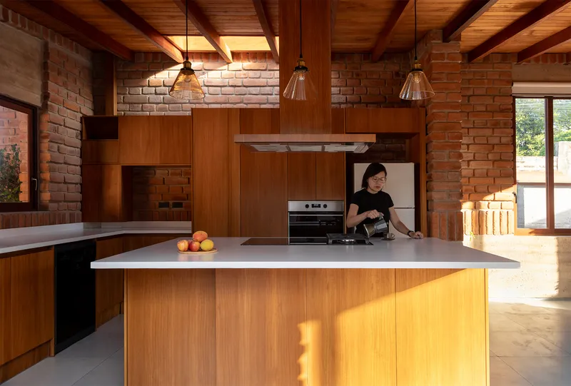 Kitchen island with timber cabinetry, pendant lights and a person preparing food under exposed beams