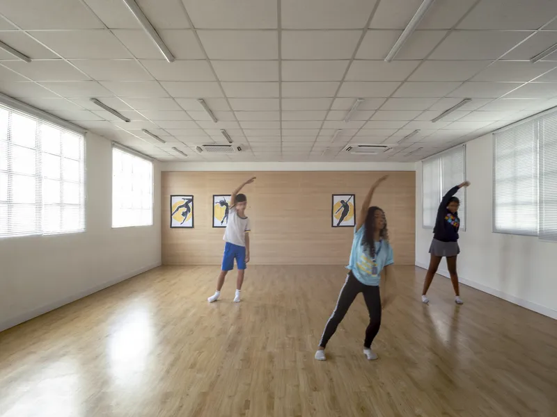 Dance studio with wood flooring and acoustic ceiling panels as three people rehearse in daylight