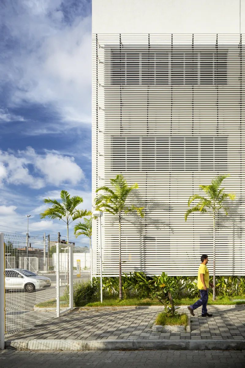 Horizontal louver facade with palm trees in a planted bed and a person walking past