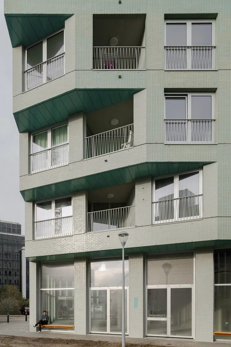 Stacked balconies with dark green canopies and metal railings above the ground-floor entrance on a cloudy afternoon