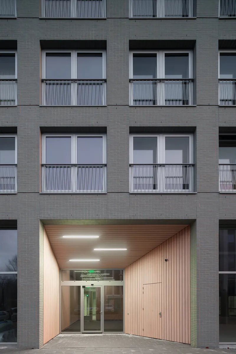 Illuminated timber-clad entrance vestibule with recessed lighting and glass doors framed by pale tile at dusk