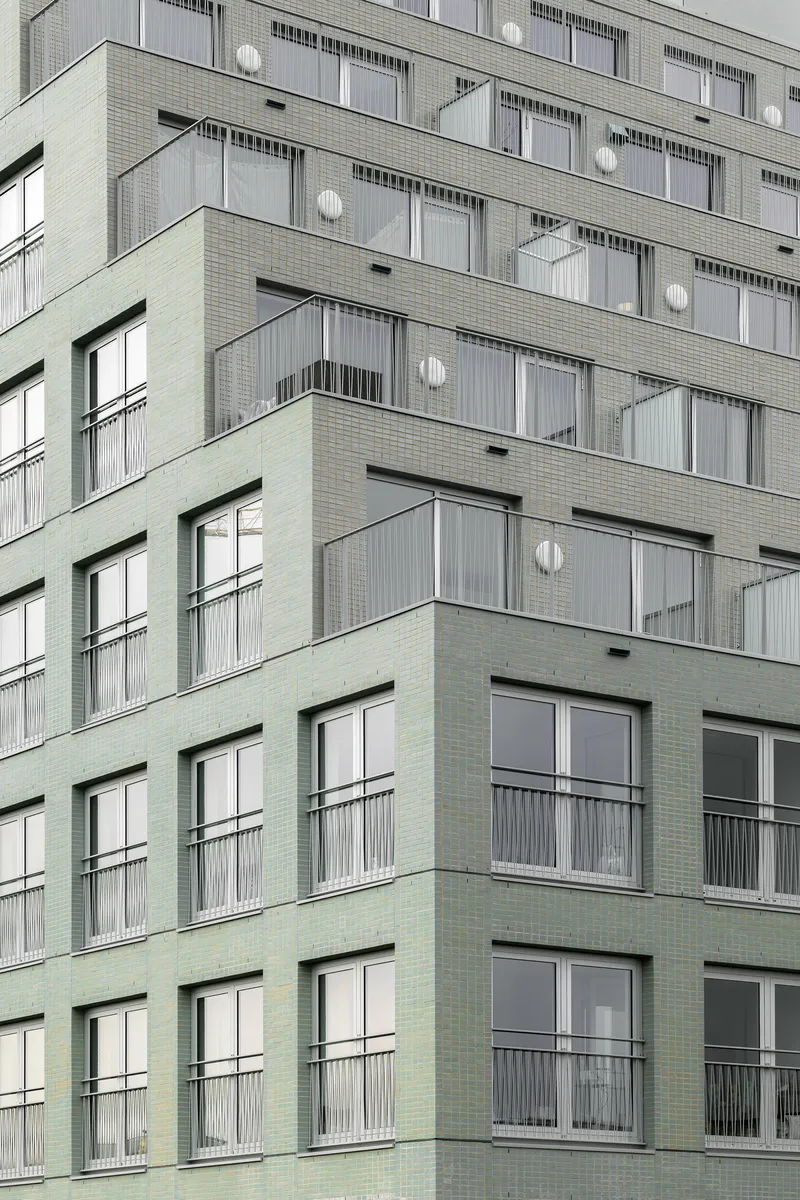 Facade detail showing alternating green and grey brick panels with recessed balconies and floor-to-ceiling windows