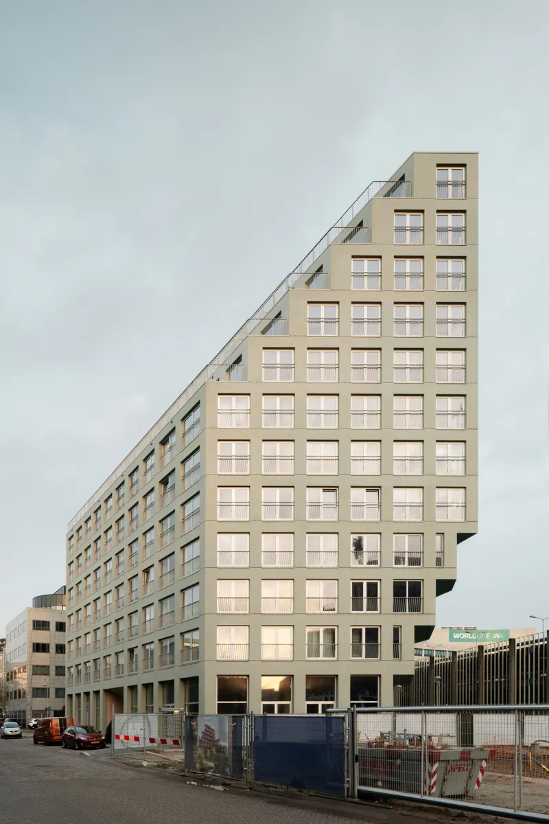 Beige brick facade with a diagonal roofline stepping down from right to left under cloudy skies