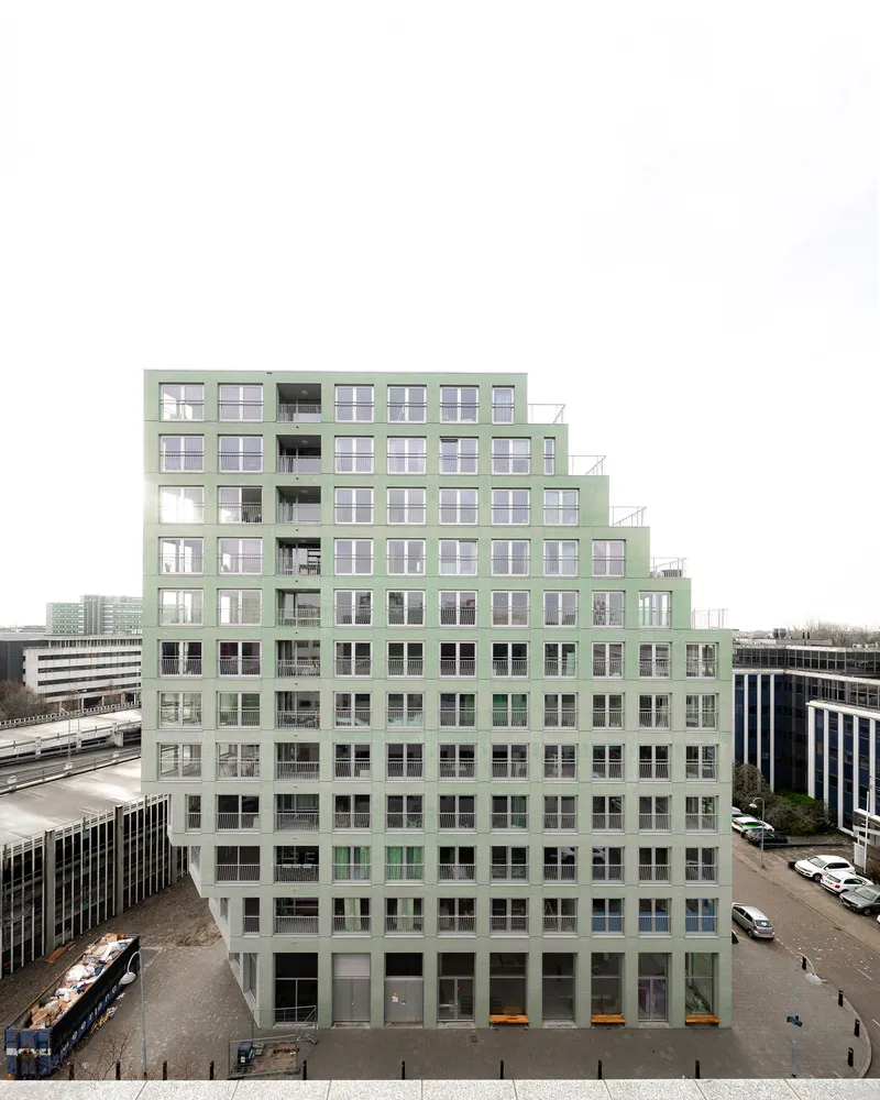 Stepped facade in pale green with recessed balconies viewed from across an adjacent roadway