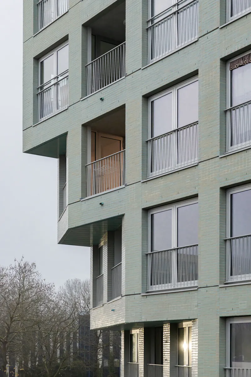 Stacked balconies with metal railings projecting from the pale green brick facade beneath bare trees