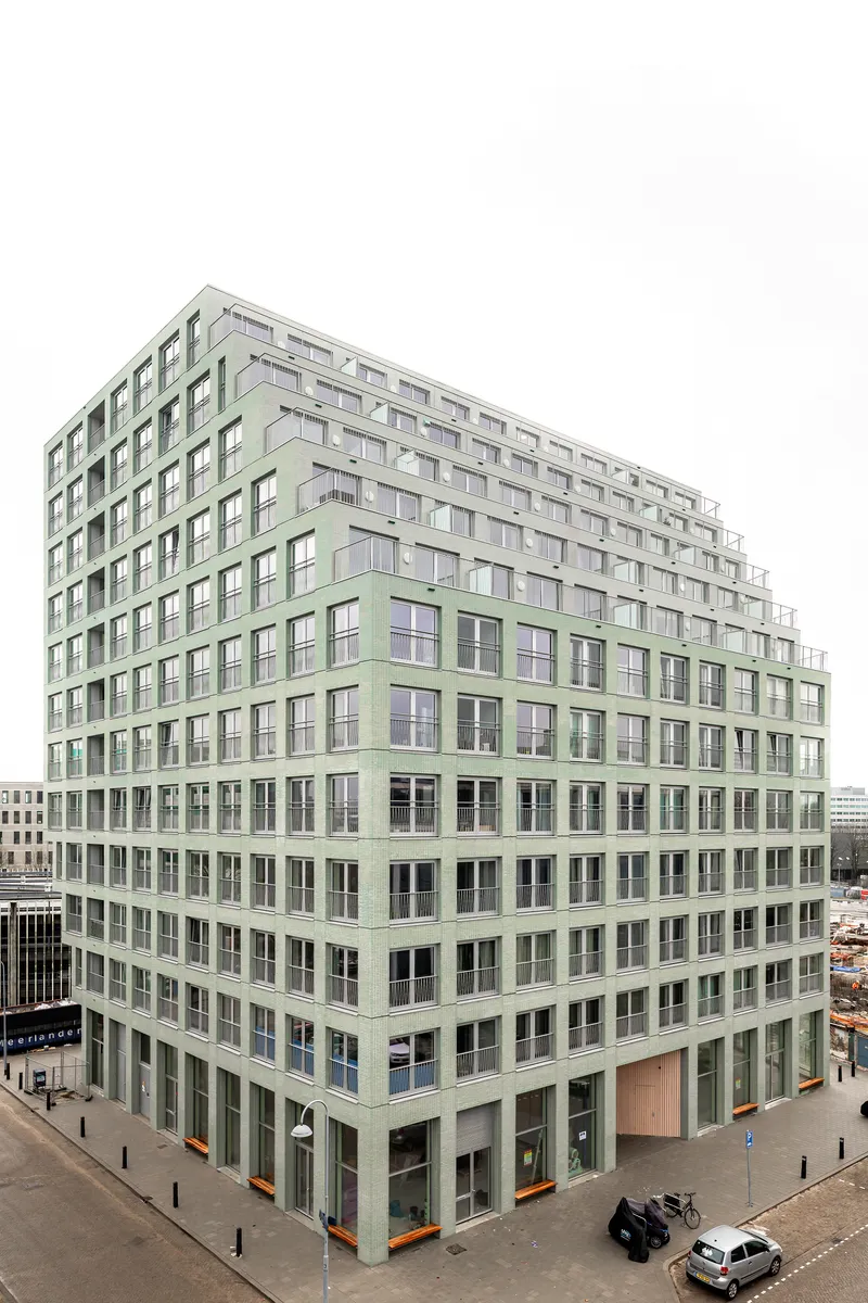 Corner elevation of the pale green facade with regular window openings and ground-level street activity