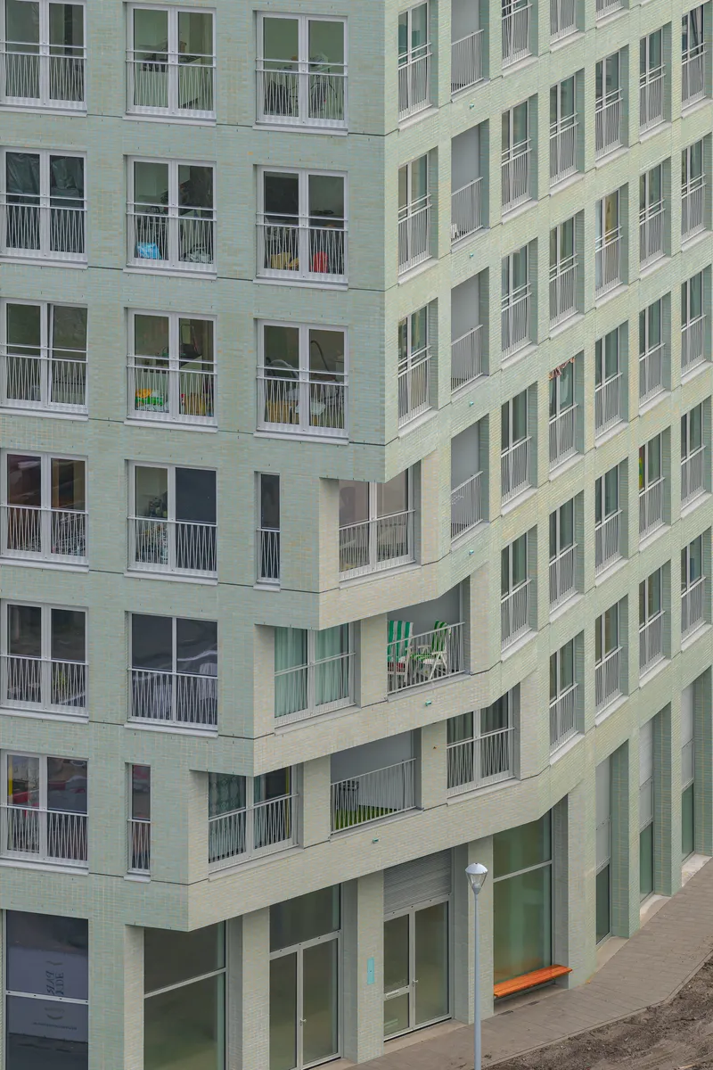 Corner courtyard view with light green brick facade, recessed balconies and ground-level glazing