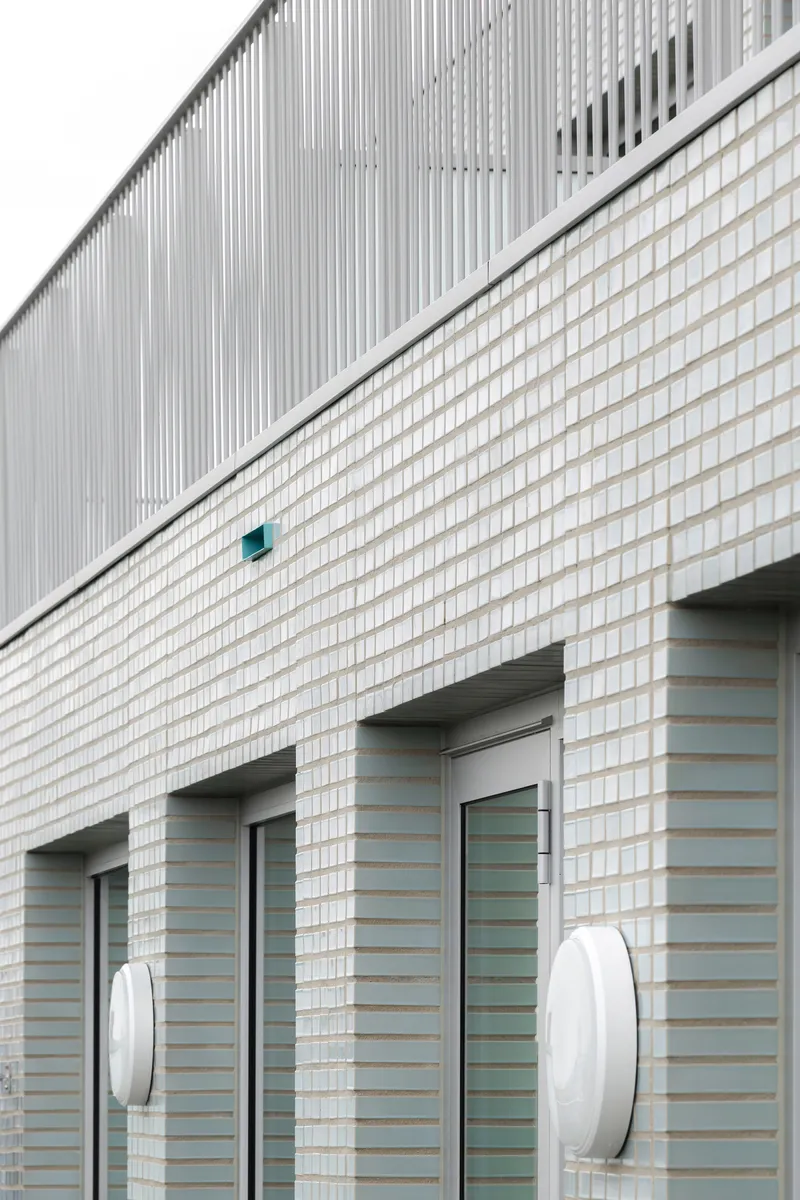 White brick facade with diagonal division line, entrance openings and circular wall-mounted light fixtures
