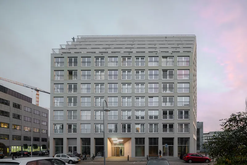 Street view of the gridded facade with rooftop pergola structure at dusk under pink sky