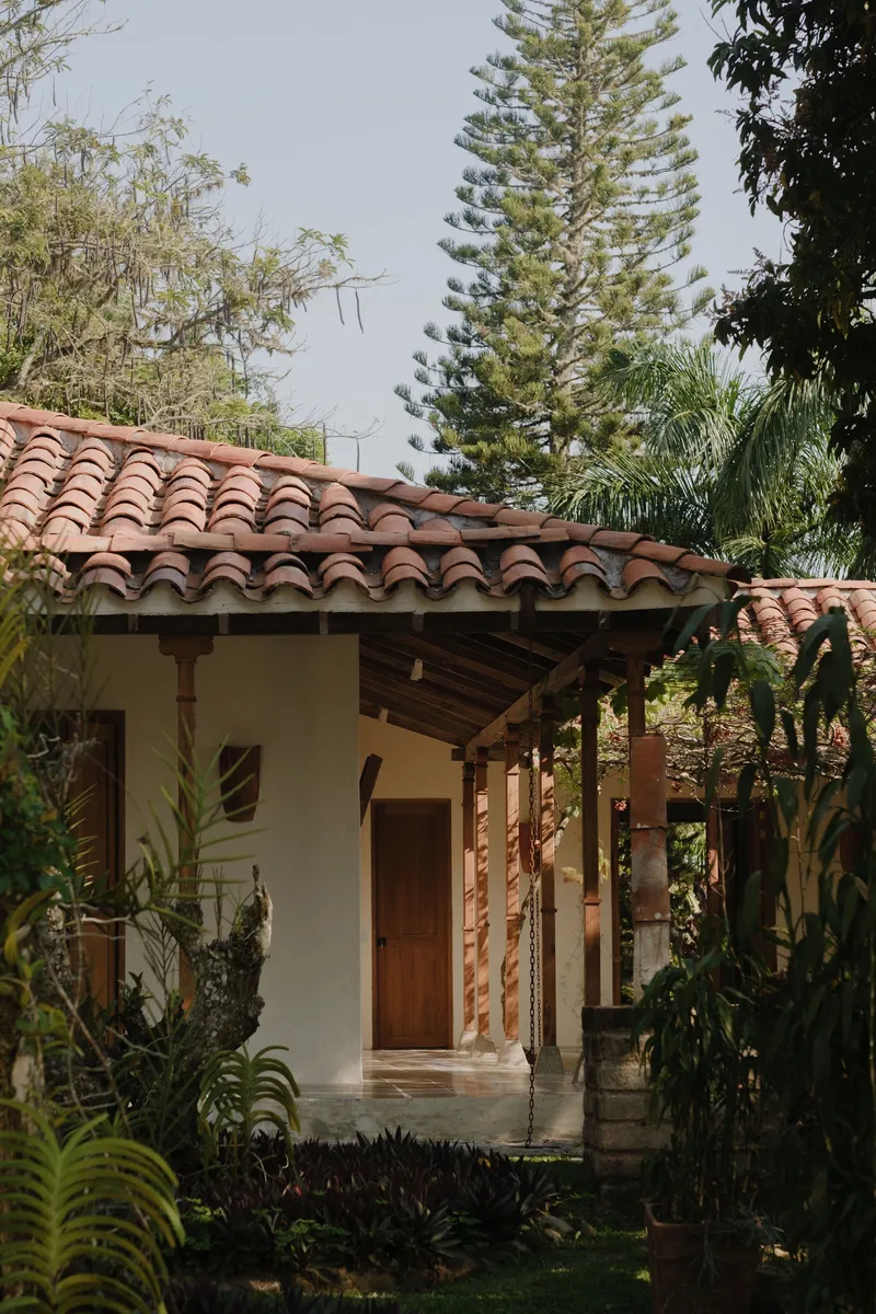 Entry facade with clay tile roof, timber porch columns, and surrounding tropical plantings