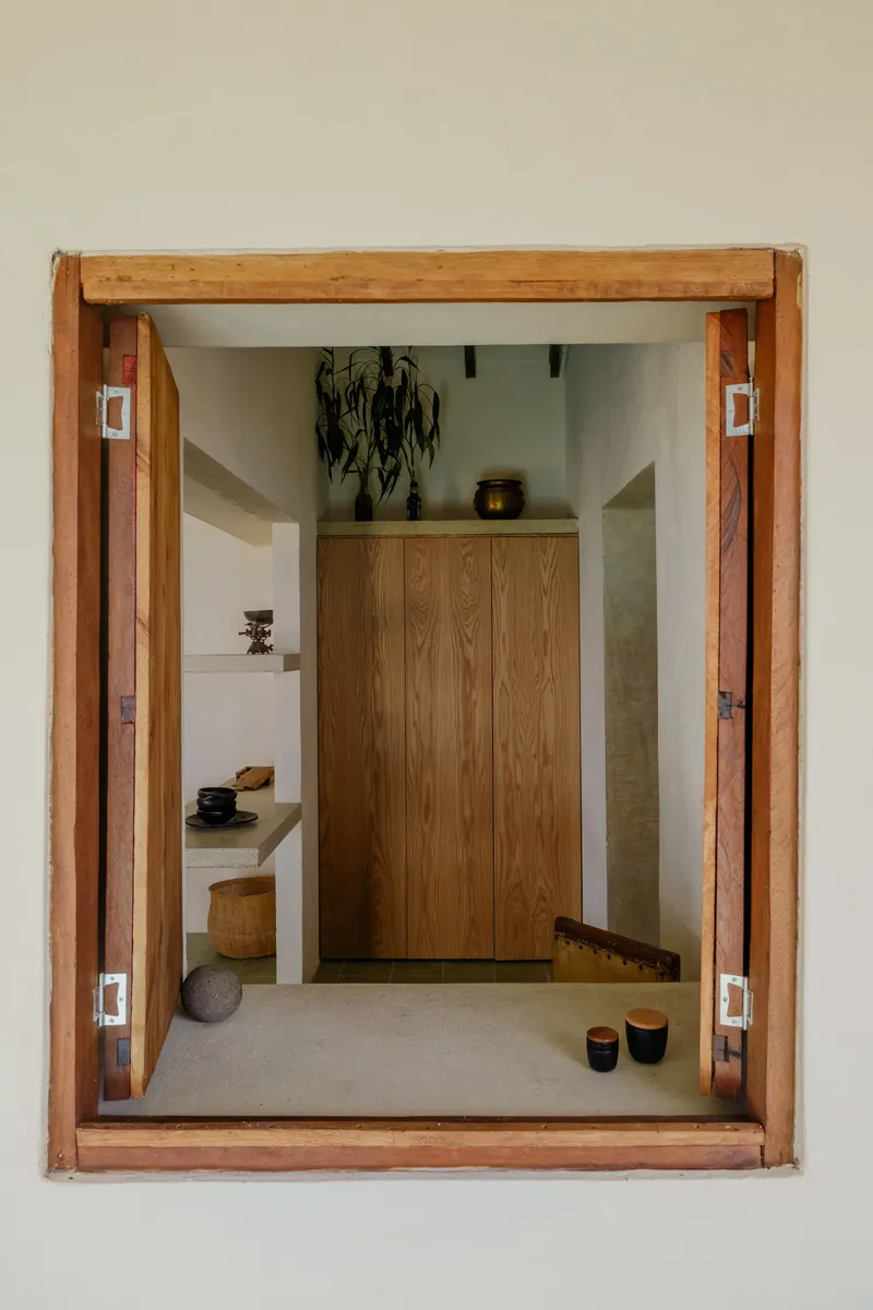 Timber-framed window opening onto interior foyer with wooden cabinet and display shelves