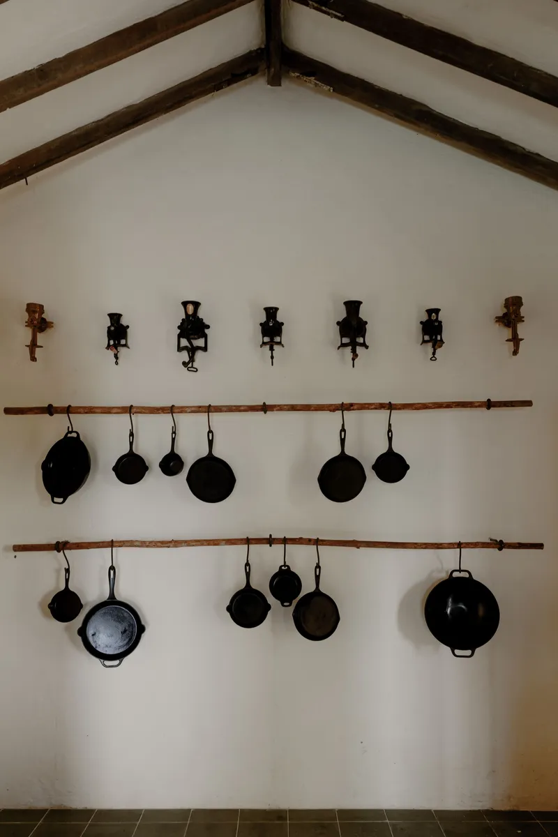 Vaulted interior wall with exposed timber beams, hanging cast iron pans and wall-mounted candle sconces