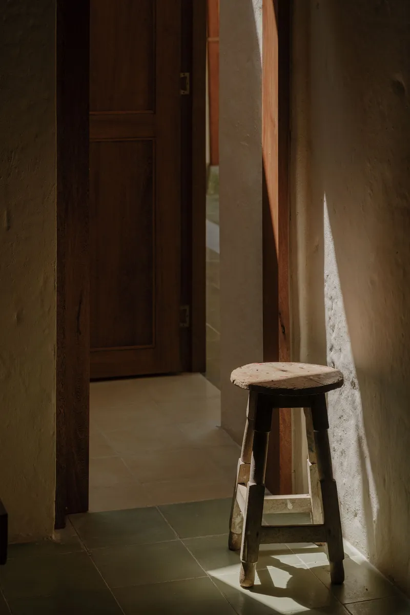 Wooden stool beside a doorway in a narrow passage with warm sunlight