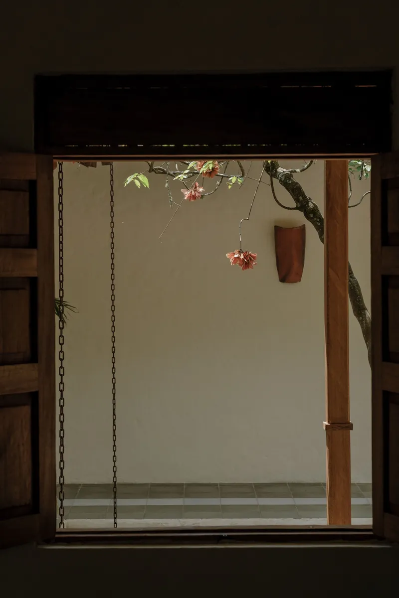 Window framing a view of a wooden column and flowering tree branch against a pale exterior wall