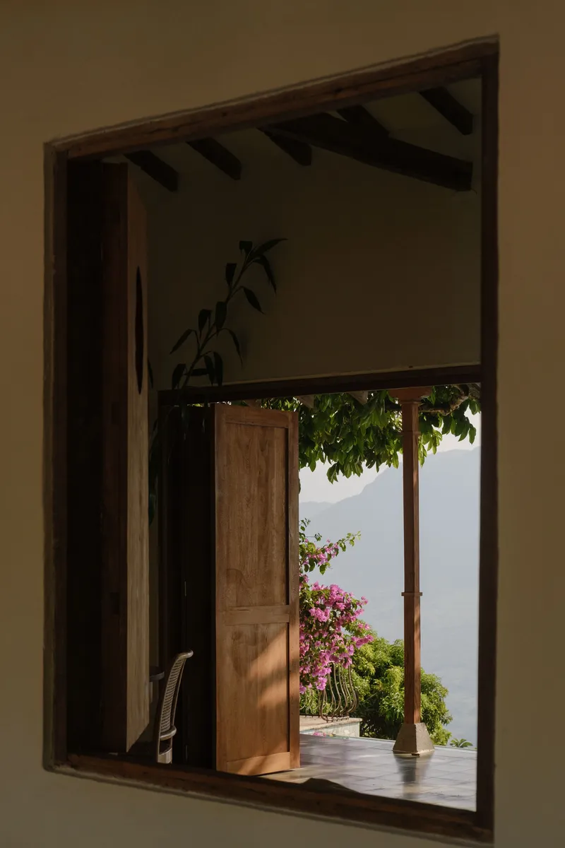 Interior window view through timber frame to terrace with bougainvillea and distant misty landscape
