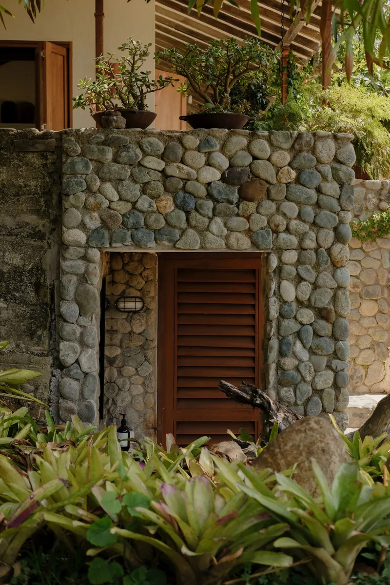 River stone wall surrounding a louvered timber door with planted bed of succulents and shrubs