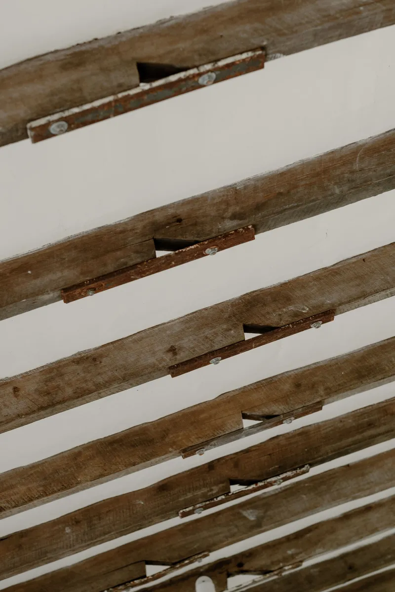 Close-up of weathered timber ceiling beams with exposed joinery and rust-stained metal connectors