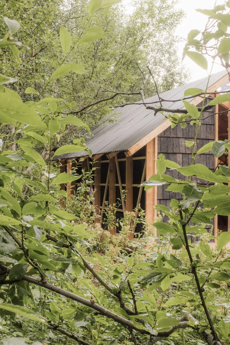 Timber-framed pavilion with corrugated metal roof partially obscured by spring foliage