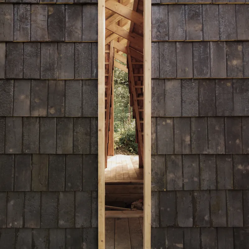 Vertical opening framed with fresh timber through weathered charred wood shingle facade