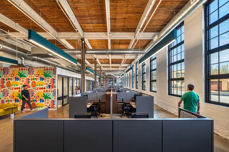 Long open-plan office corridor with timber ceiling, white trusses, workstations and colorful graphic mural