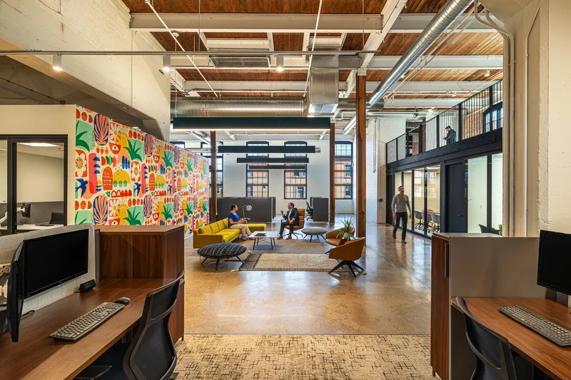 Open office lounge with exposed timber ceiling, pendant lights, and a colorful patterned mural wall