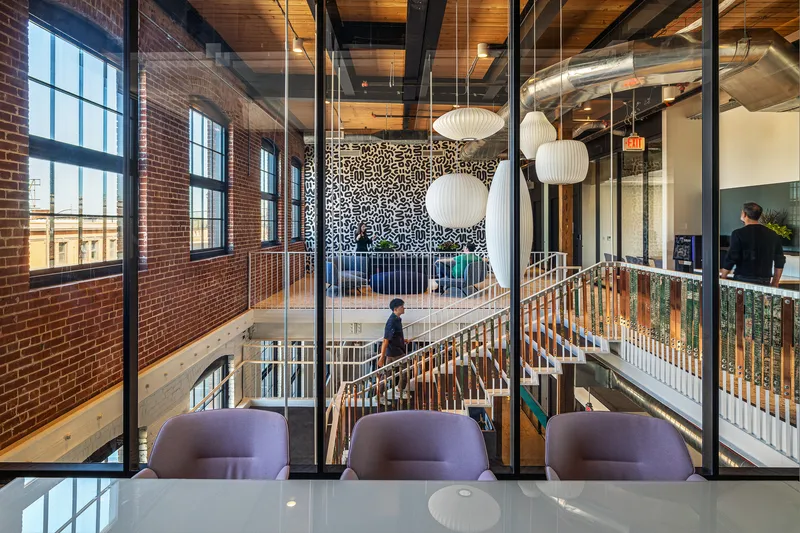 Upper-level meeting room overlooking an open stairwell with timber railings and pendant lamps