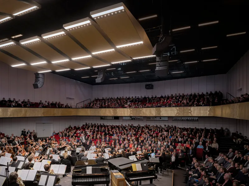 Concert hall auditorium with tiered seating filled with audience members and orchestra on stage