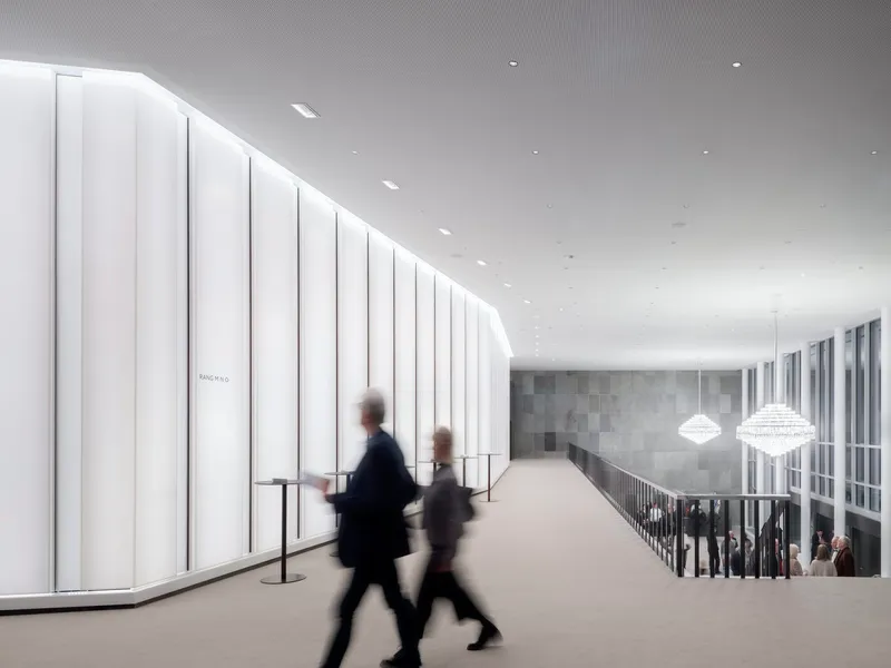 Upper-level corridor with vertical white panels along one wall and two blurred figures walking