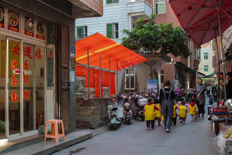 View of the orange canopy from the adjacent street with children and motorbikes passing by