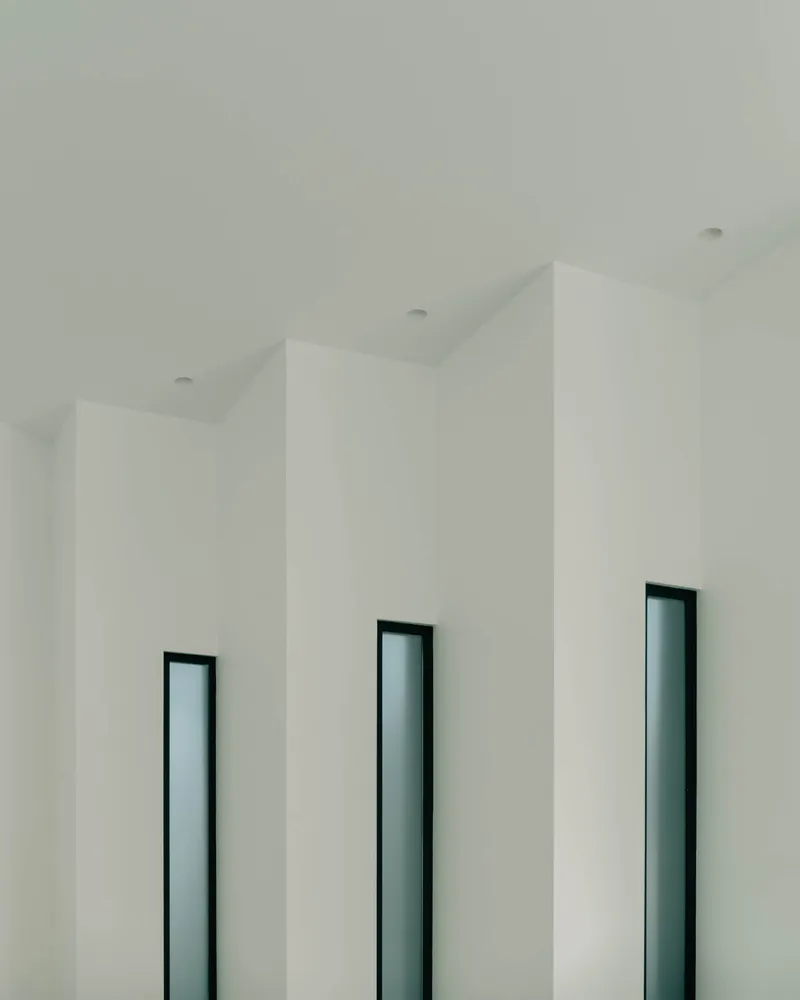 Three vertical window openings with dark frames set into white folded ceiling planes