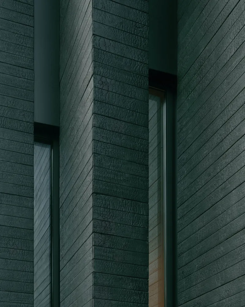 Close-up of horizontal timber cladding meeting at a recessed corner with narrow window openings