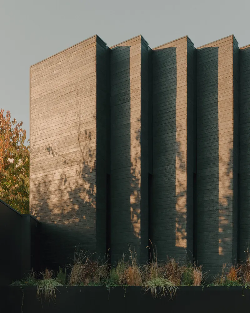 Sawtooth timber facade with alternating light and shadow planes at golden hour above planted bed