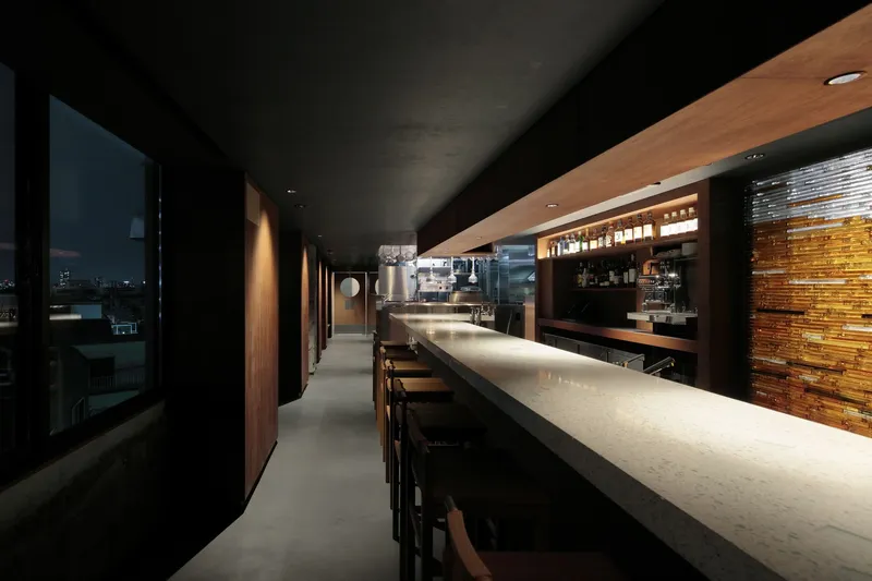 Long bar counter with embedded lighting leading toward illuminated timber screen wall and kitchen area
