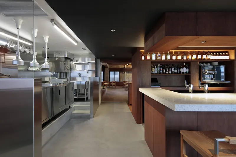 Restaurant interior with stainless steel kitchen equipment and walnut bar counter under linear ceiling lights