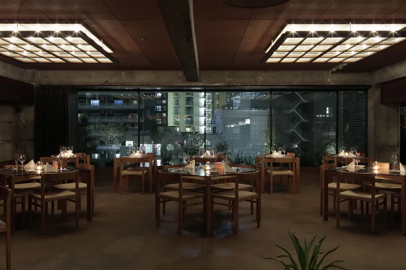 Dining room with wooden tables set for service beneath illuminated ceiling panels at night