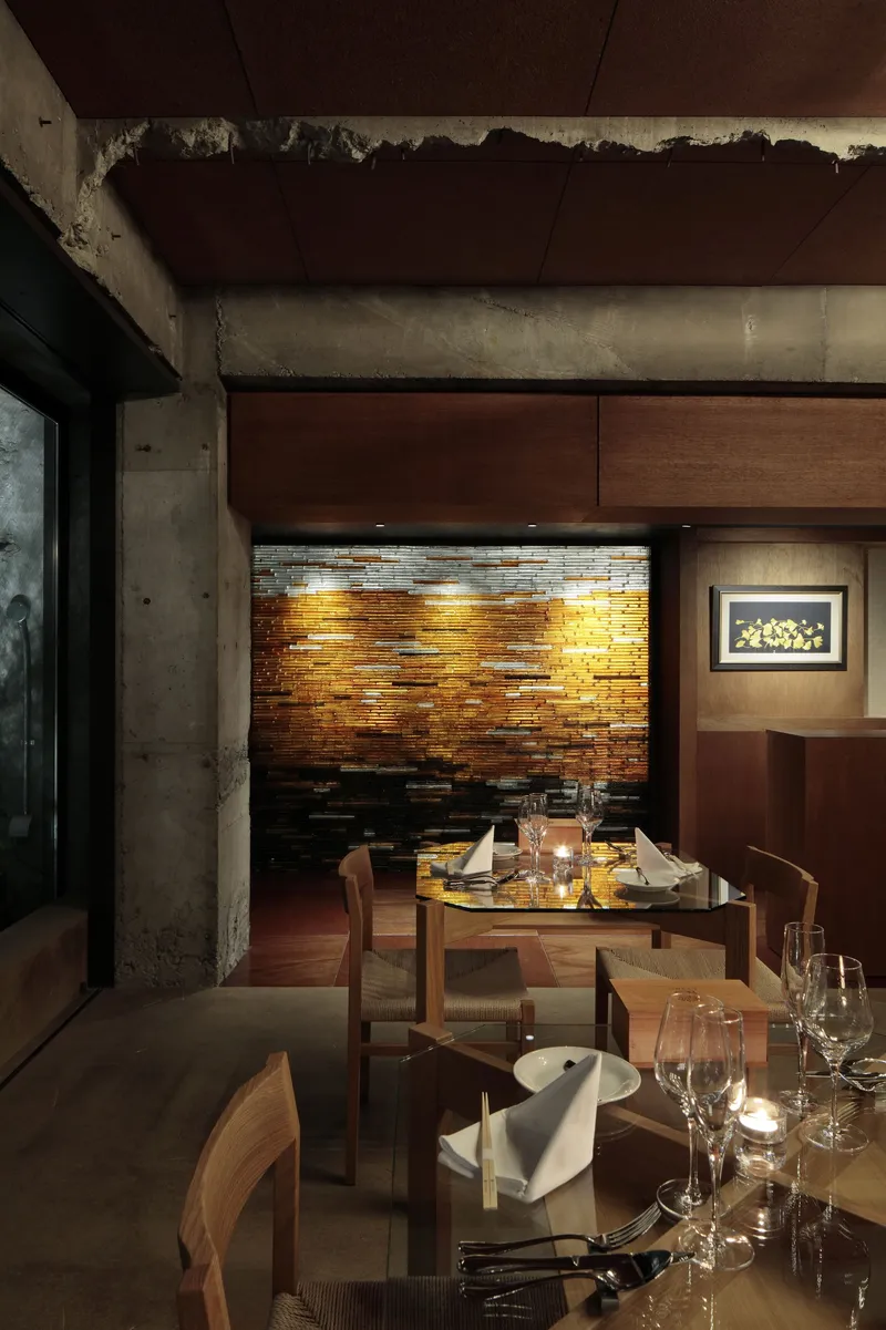 Dining area featuring copper tile accent wall and exposed concrete beam with candlelit tables