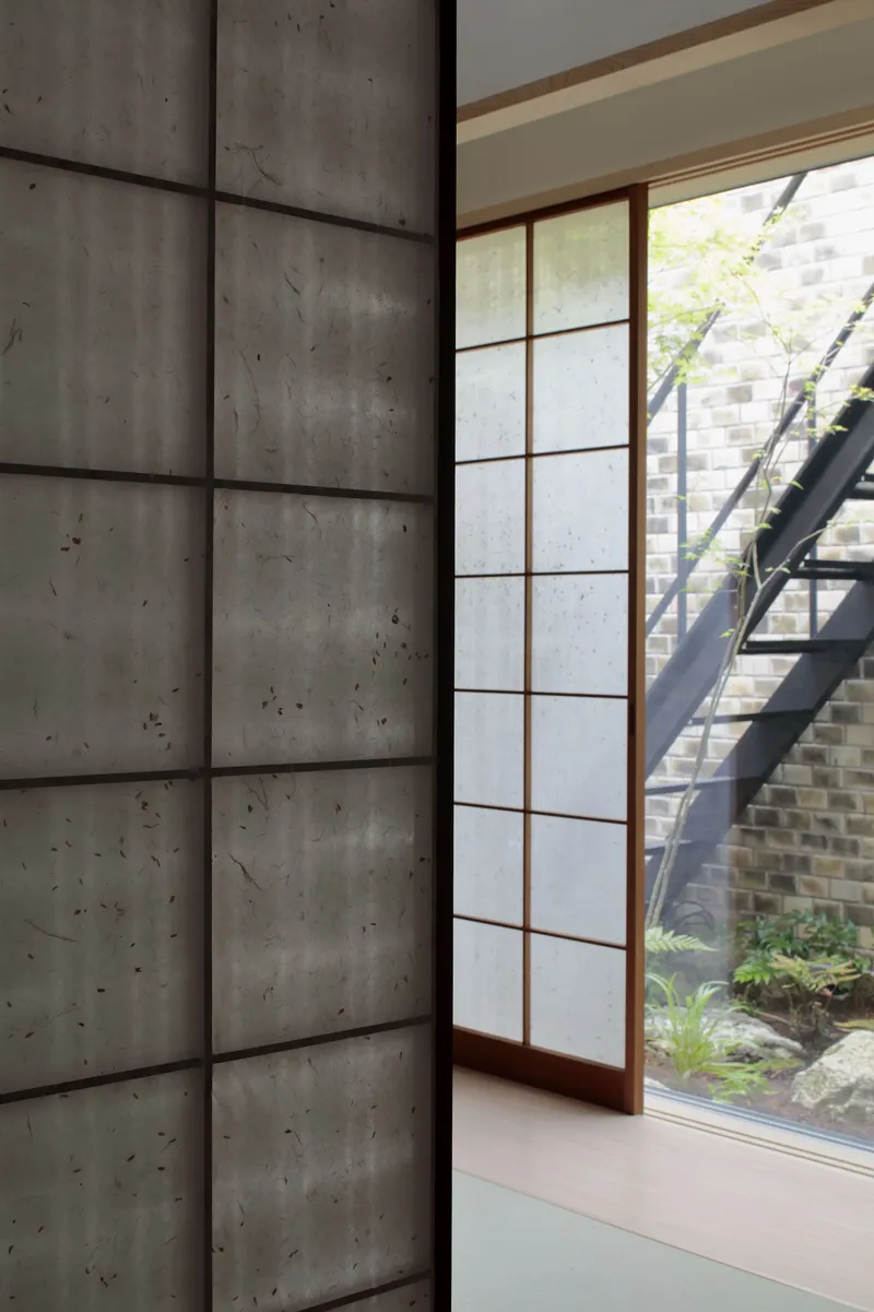 Shoji screen and board-formed concrete wall beside a courtyard garden with steel stair