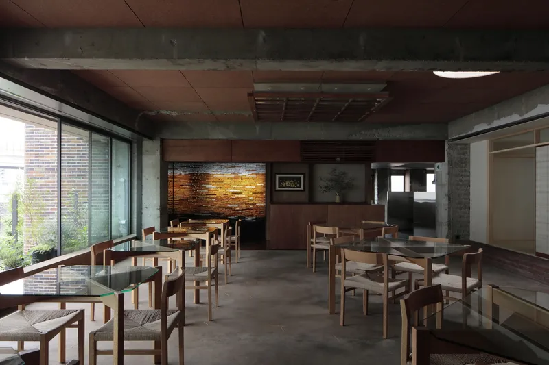 Dining area with timber tables and chairs beneath exposed concrete beams and reddish ceiling panels