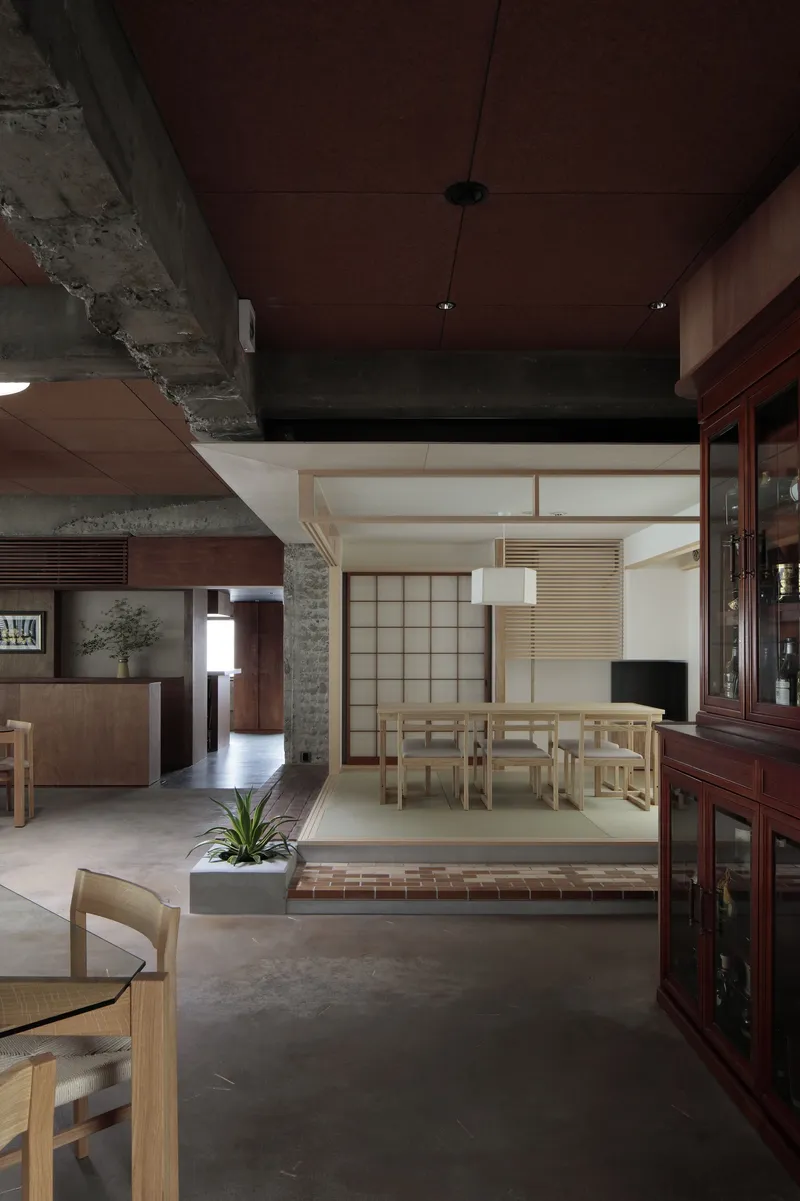 Interior view showing raised tatami room with shoji screens behind exposed concrete beams and dark wood ceiling