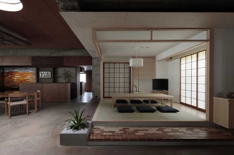 Elevated tatami platform with floor cushions and translucent sliding panels framed by raw concrete structure