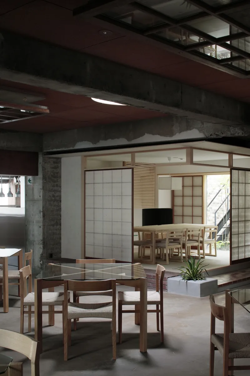 Dining area with timber chairs and tables beneath gridded ceiling fixture and exposed concrete beams