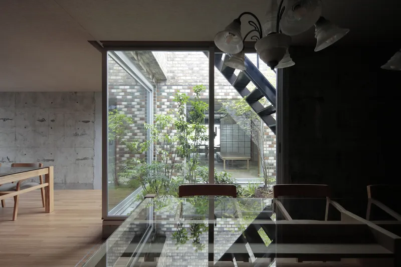 Interior courtyard with glass block walls and planted trees viewed through floor-to-ceiling glazing and steel staircase