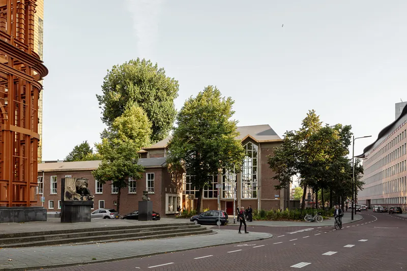 Street view of the brick facade with arched glazing and mature trees in dappled afternoon light