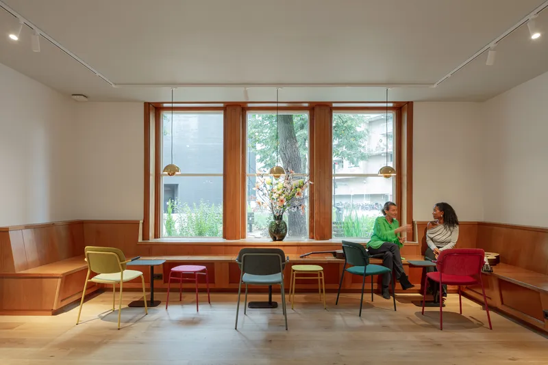 Interior gathering room with timber-framed windows, built-in bench seating, and two people in conversation