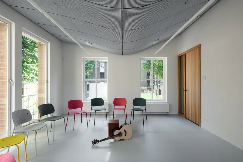 Practice room with curved acoustic ceiling panels, colored chairs arranged in semicircle, and acoustic guitar