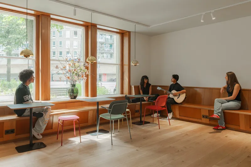 Lounge area with timber built-in seating along windows and people with guitar in afternoon light
